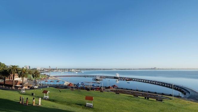 Geelong foreshore Grassy area in front of a beach with a semi-circular pier and city skyline in the distance
