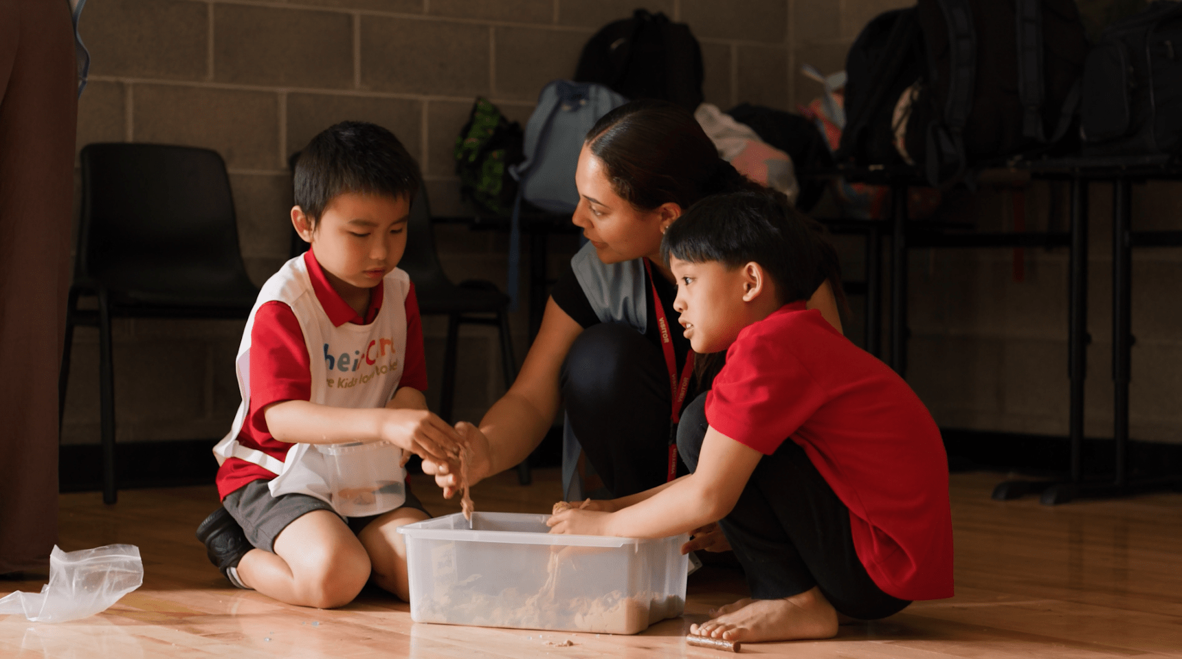 Two students as part of OSHC program crouching down and playing alongside a teacher